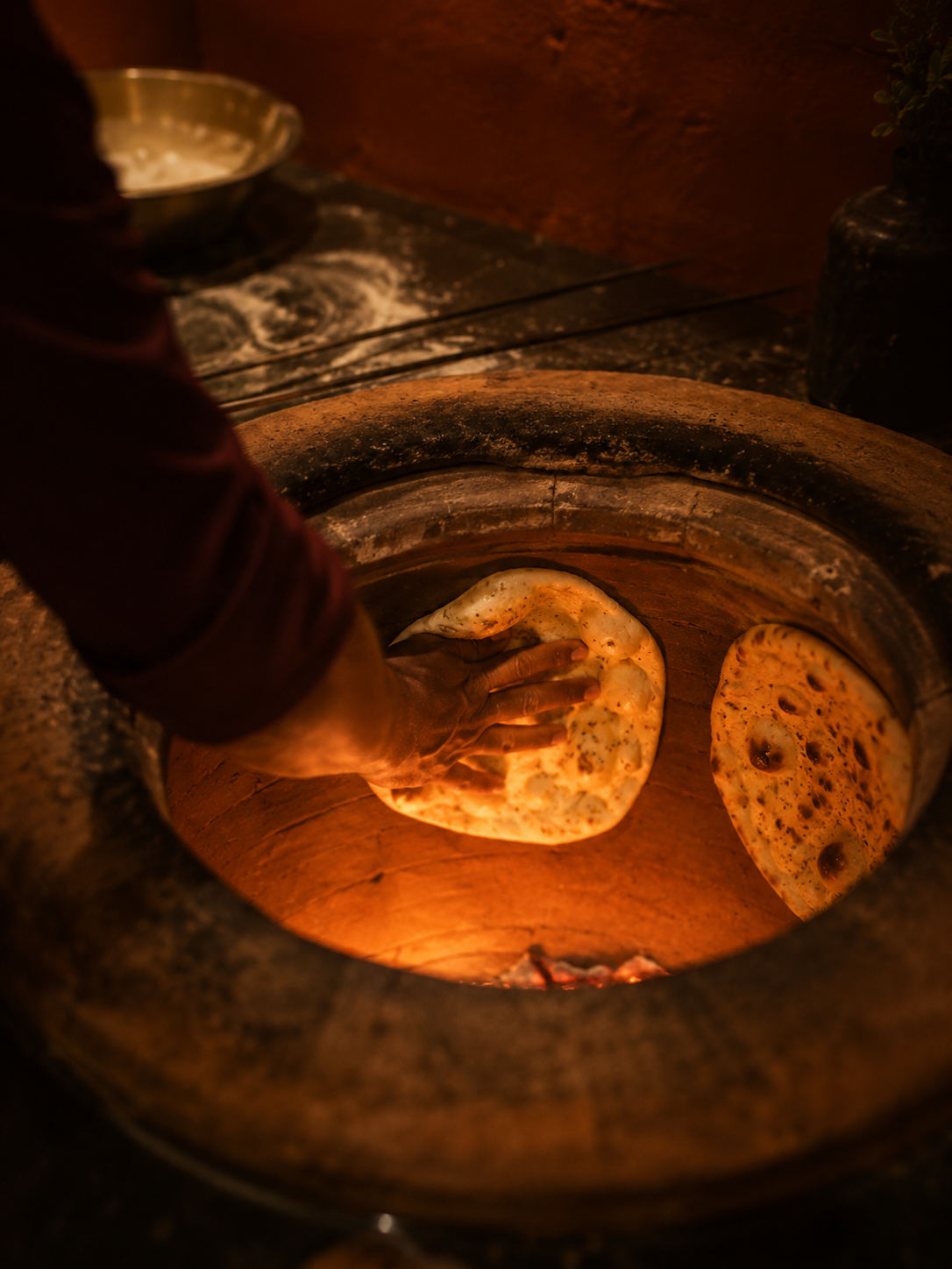 Hand pressing naan against the hot clay wall of a tandoor